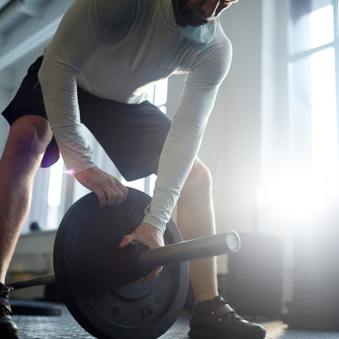A man preparing to approach the barbell pull exercise by leaning over the edge of the barbell.